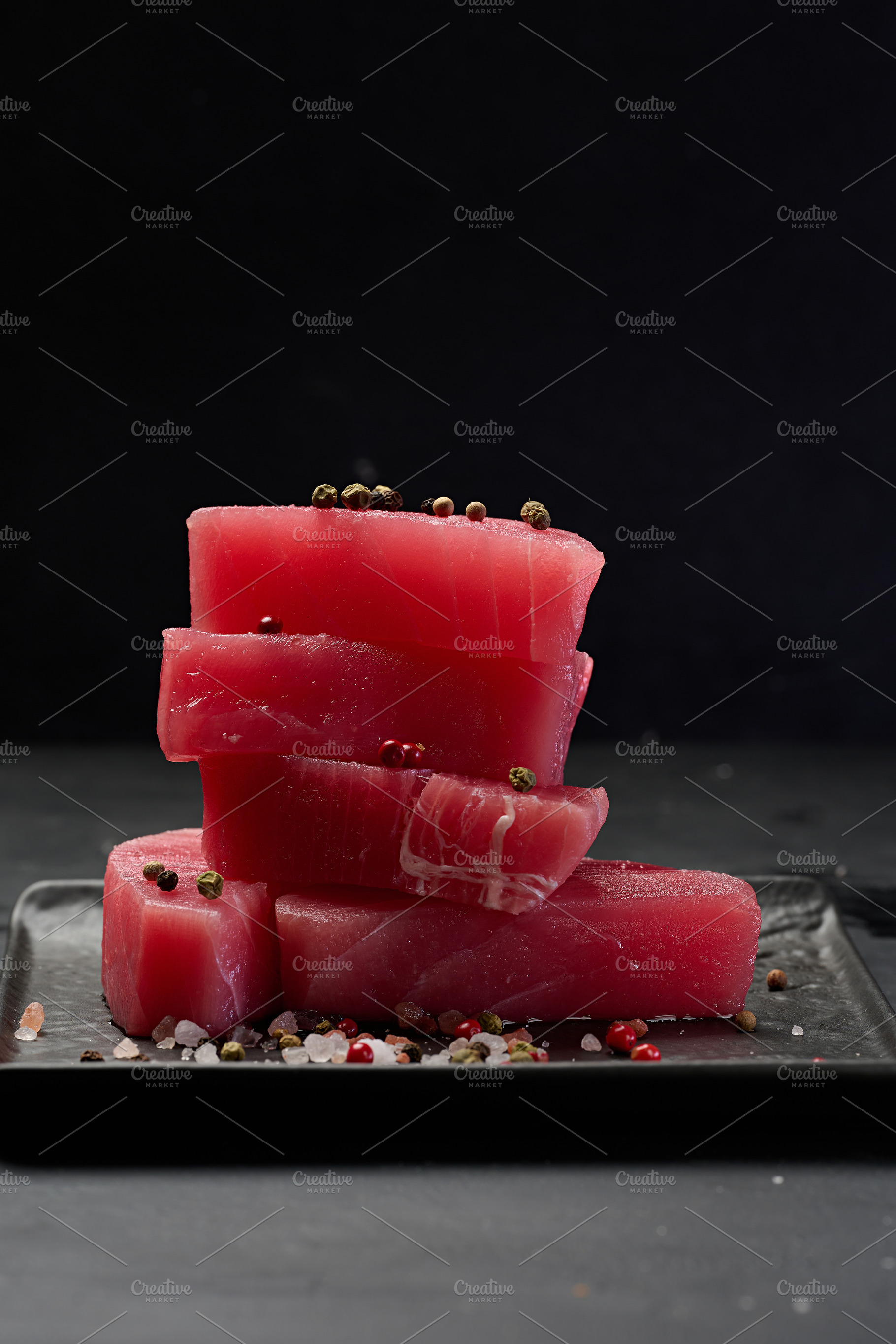 Stack of raw tuna pieces on black square plate, black background, a Food & Drink Photo by ndanko