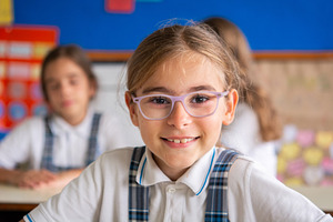 Smiling schoolgirl with glasses looking at camera in classroom, a Person Photo by etorres69