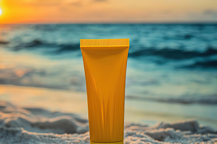 Yellow sunscreen tube on white sandy beach at sunset near ocean waves, a Beauty & Fashion Photo by AlyaAnd