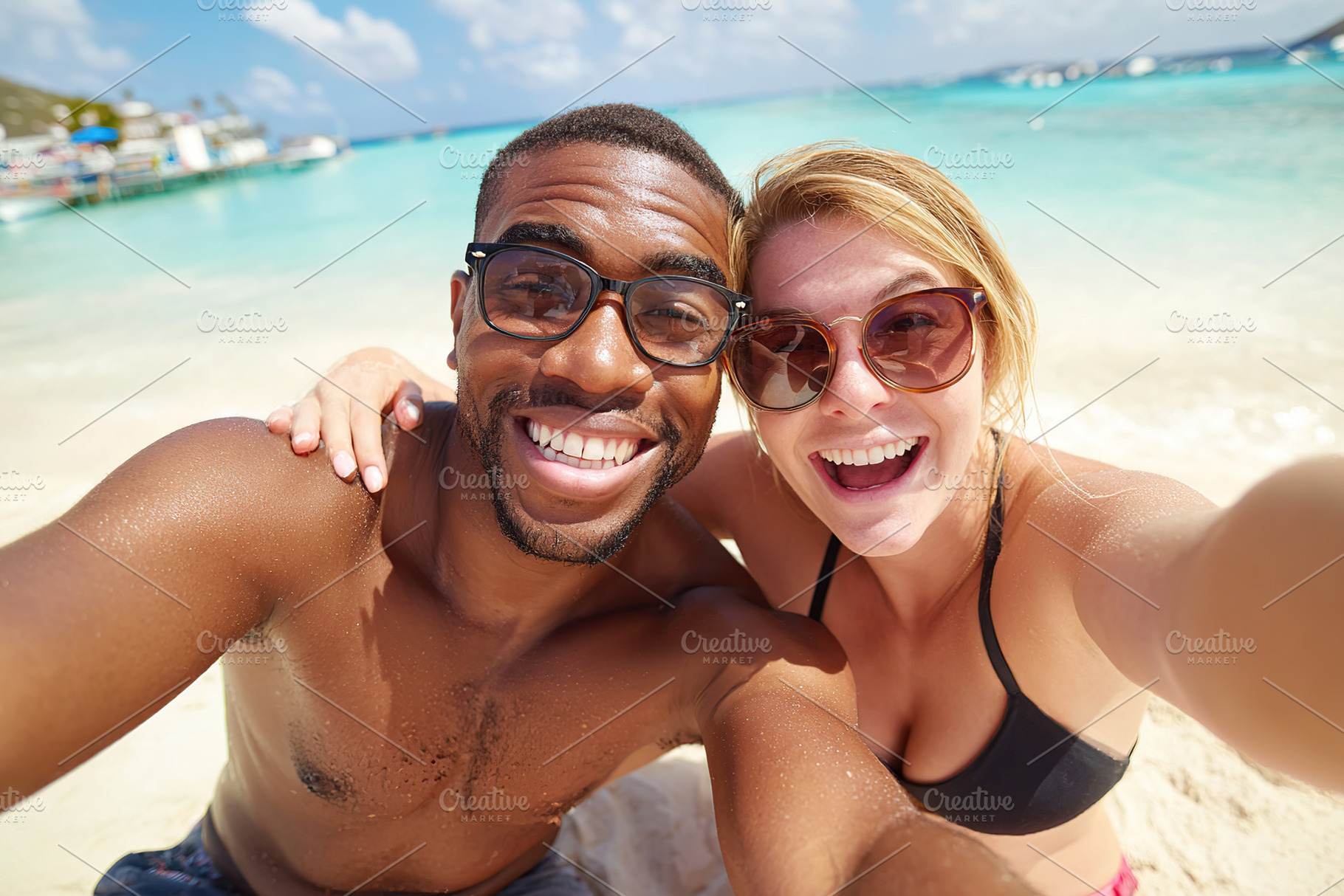 Happy couple enjoying a sunny day at the beach while taking a joyful selfie, a Photo by AlyaAnd