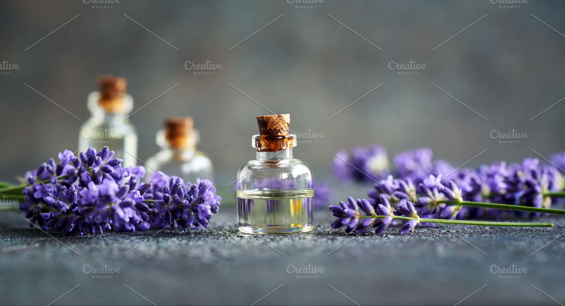 A bottle of essential oil with blooming lavender plant on gray b, a Food & Drink Photo by Madeleine Steinbach