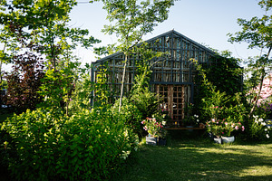 Cozy wooden greenhouse surrounded by lush green plants and colorful flowers, a Photo by AS photostudio