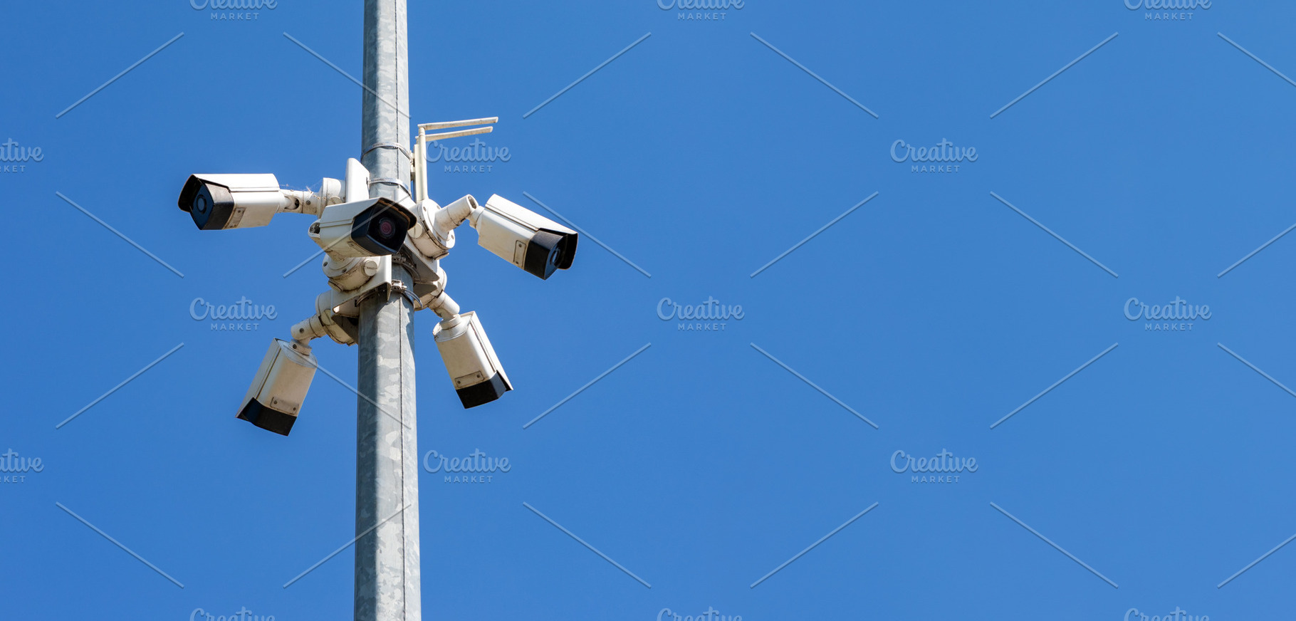 Multiple security cameras mounted on a pole against clear blue sky, symbolizing, an Industrial Photo by Ales Munt