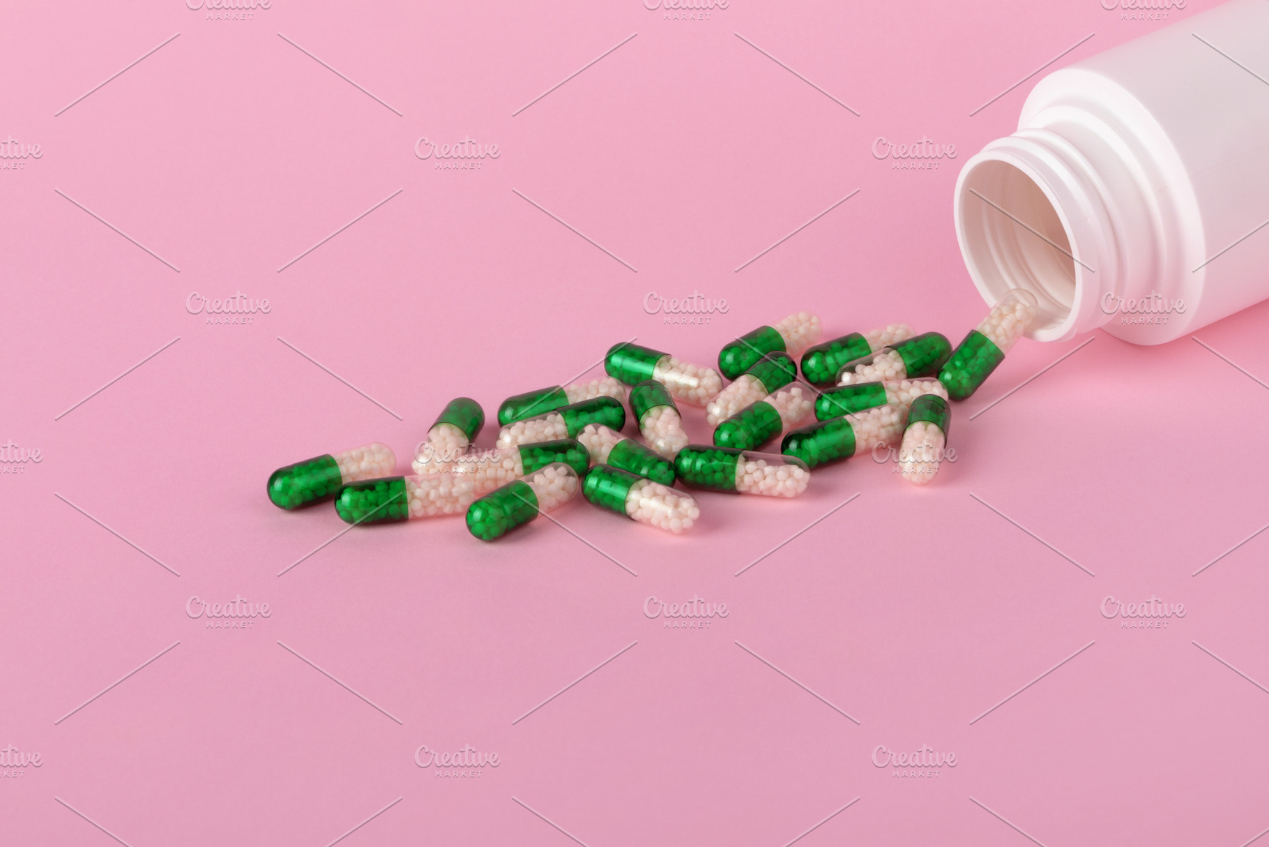 Green and white capsules spilling from a white bottle onto a pas, a Health & Medical Photo by Ales Munt