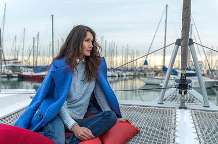 Beautiful woman in pink dress and blue jacket posing on a sailboat in a city ha