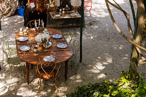 Wooden outdoor table in a garden courtyard set with vintage plates, a Food & Drink Photo by Bepslabor