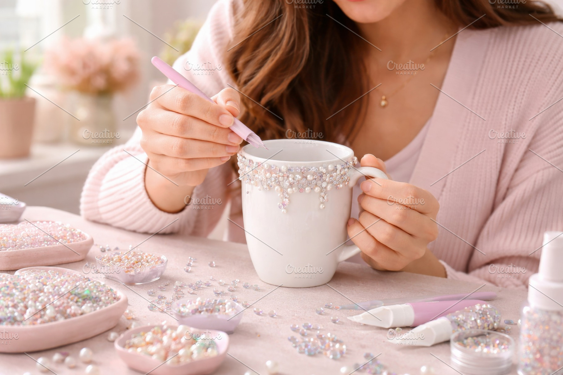 Woman decorating mug with crystals at home, craft concept, a Photo by Dvoevnore photos