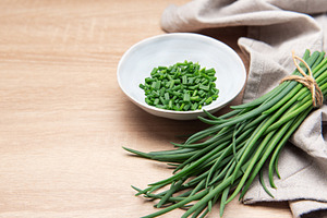Freshly cut chives in a bowl resting on wooden table, a Photo by Olena Rudo