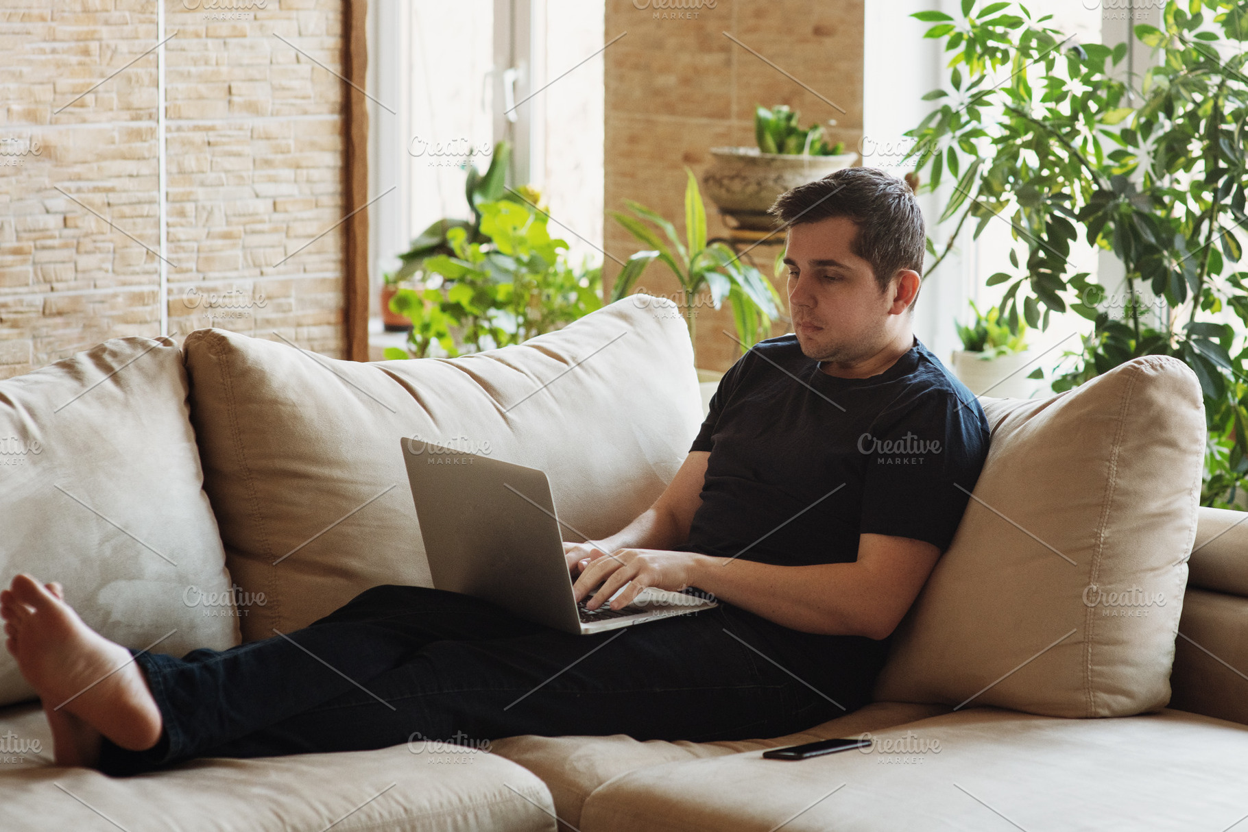 Man lying on sofa and working on his, a Person Photo by Aliona Serzhanova