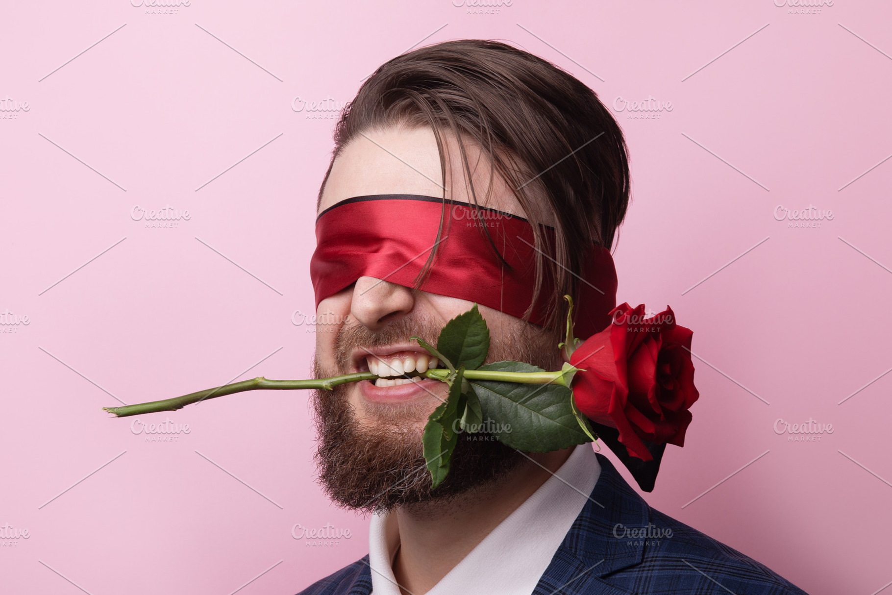 Bearded man in a suit wearing a red blindfold, biting a red rose, a Person Photo by Ales Munt