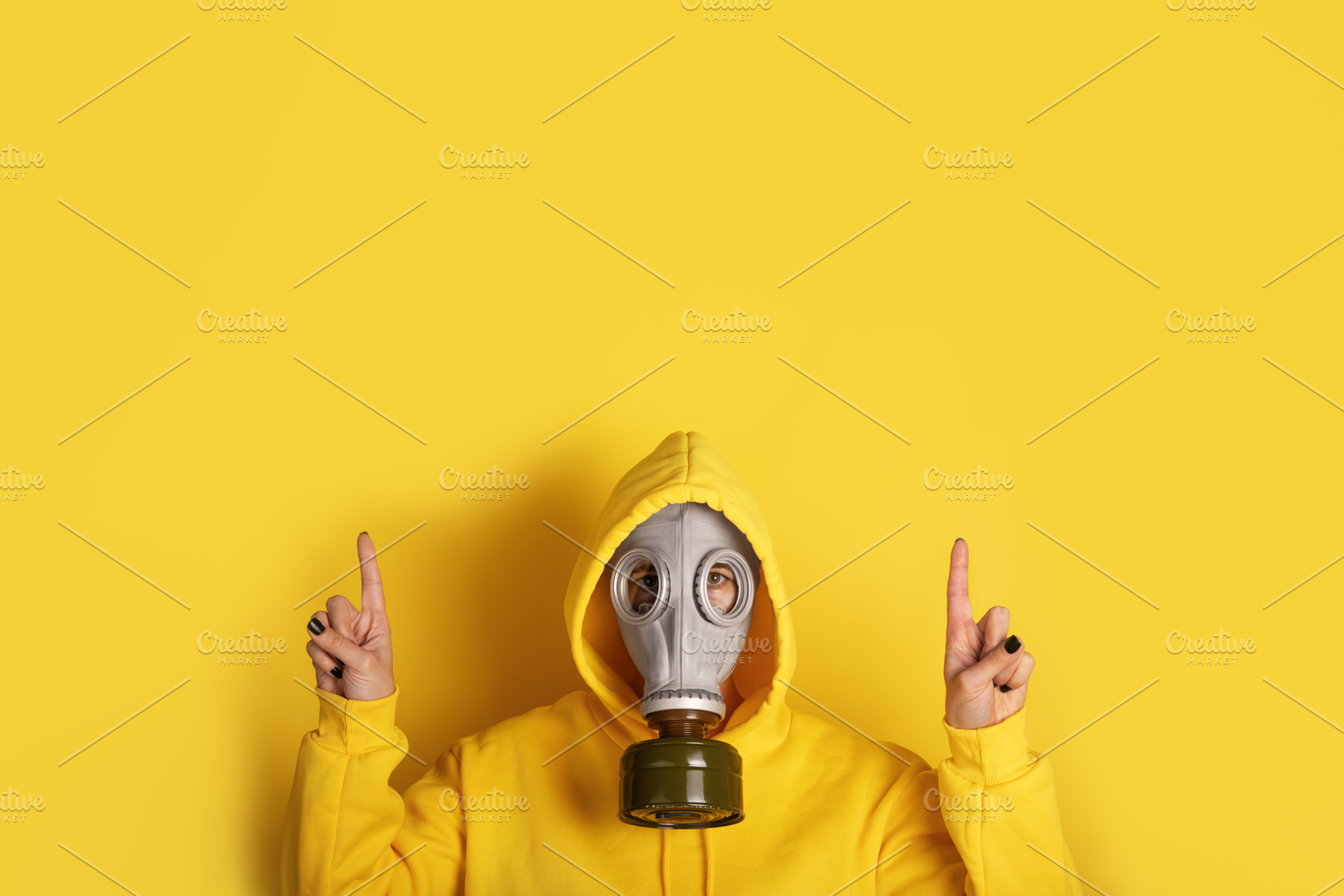 Individual in yellow hoodie and gas mask pointing upwards agains, a Person Photo by Ales Munt