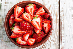 Pieces of strawberries in bowl on wooden table, a Food & Drink Photo by AlyaAnd