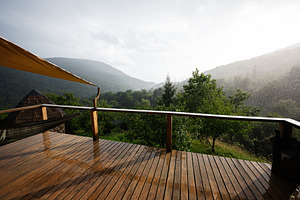 Wooden deck overlooking lush misty green valley under gentle rainfall, a Photo by AS photostudio