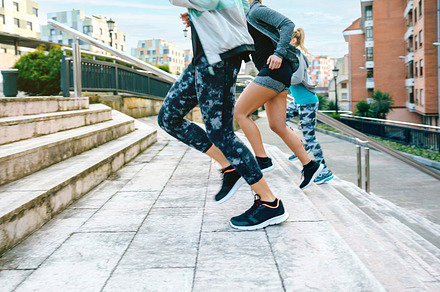 Young women friends training running up stairs in town