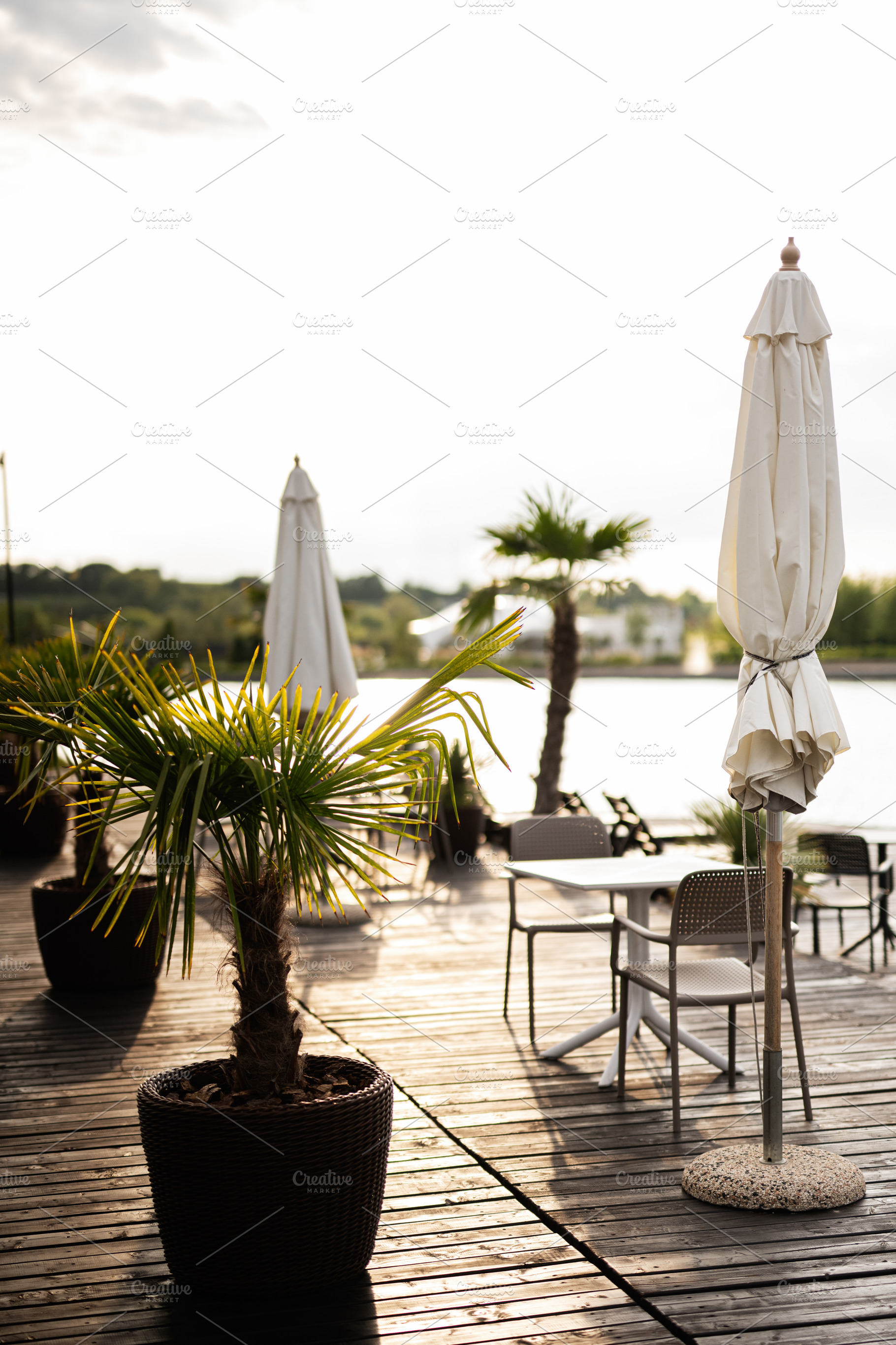 Outdoor patio with chairs, umbrellas, and planters near a scenic water view, a Photo by AS photostudio
