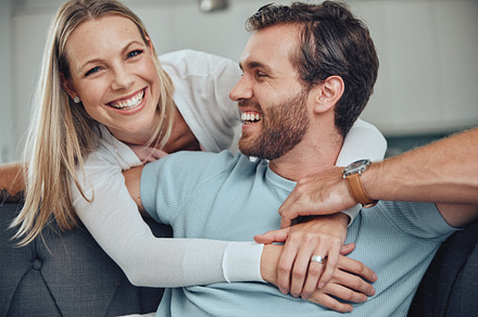 Portrait, love and couple relax on a sofa, embrace and smile while bonding in their home together. Face, man and woman  hug, happy and enjoy quality time, relationship and fun in their living room, a Photo by Peopleimages.com
