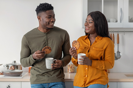 Portrait Of Happy Black Couple Drinking Coffee And Eating Cookies In Kitchen, a Photo by Prostock-Studio