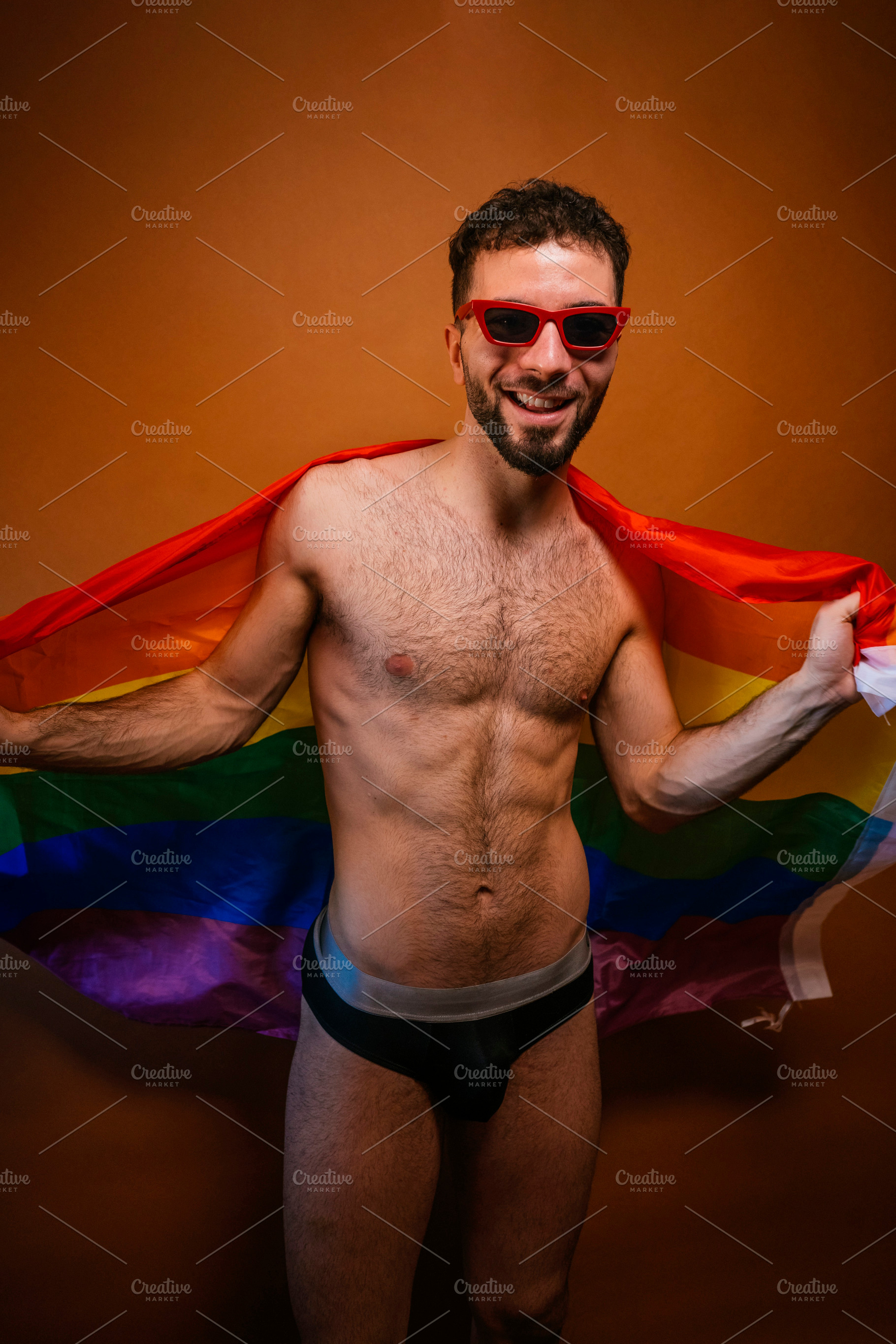 Young adult man smiling at camera holding a rainbow flag, a Photo by karrastock