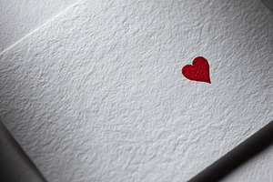 Minimal white textured card showing small red heart, symbolizing, a Photo by Studio ANNA