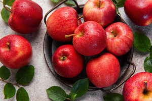 Fresh red apples with green leaves resting in a metal basket, a Food & Drink Photo by Olena Rudo