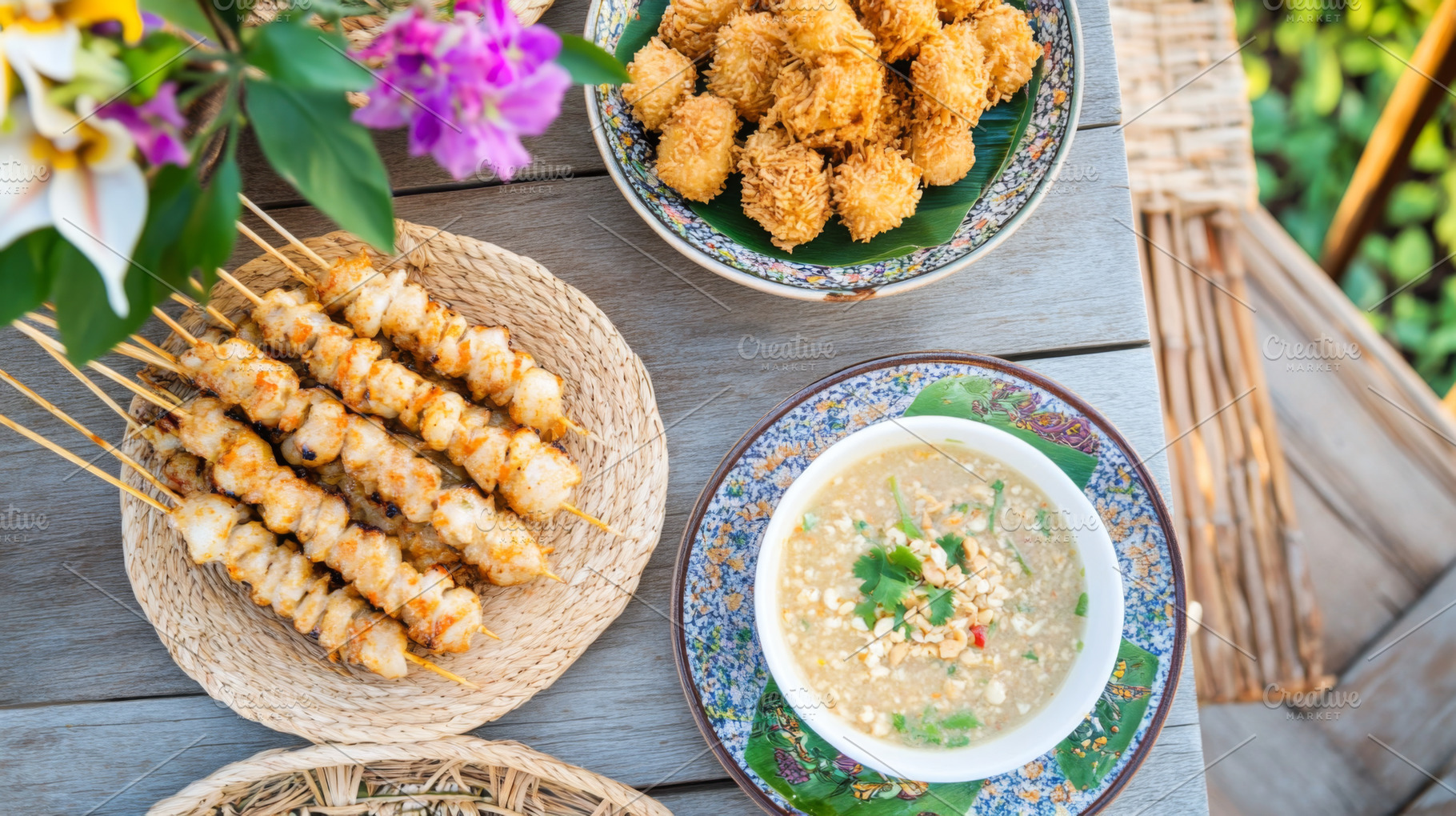 Satay skewers and shrimp with rice, sauces, and orchids arranged, a Photo by Dvoevnore photos