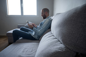 Man using smartphone sitting on sofa at home, relaxed lifestyle with copy space, a Person Photo by etorres69