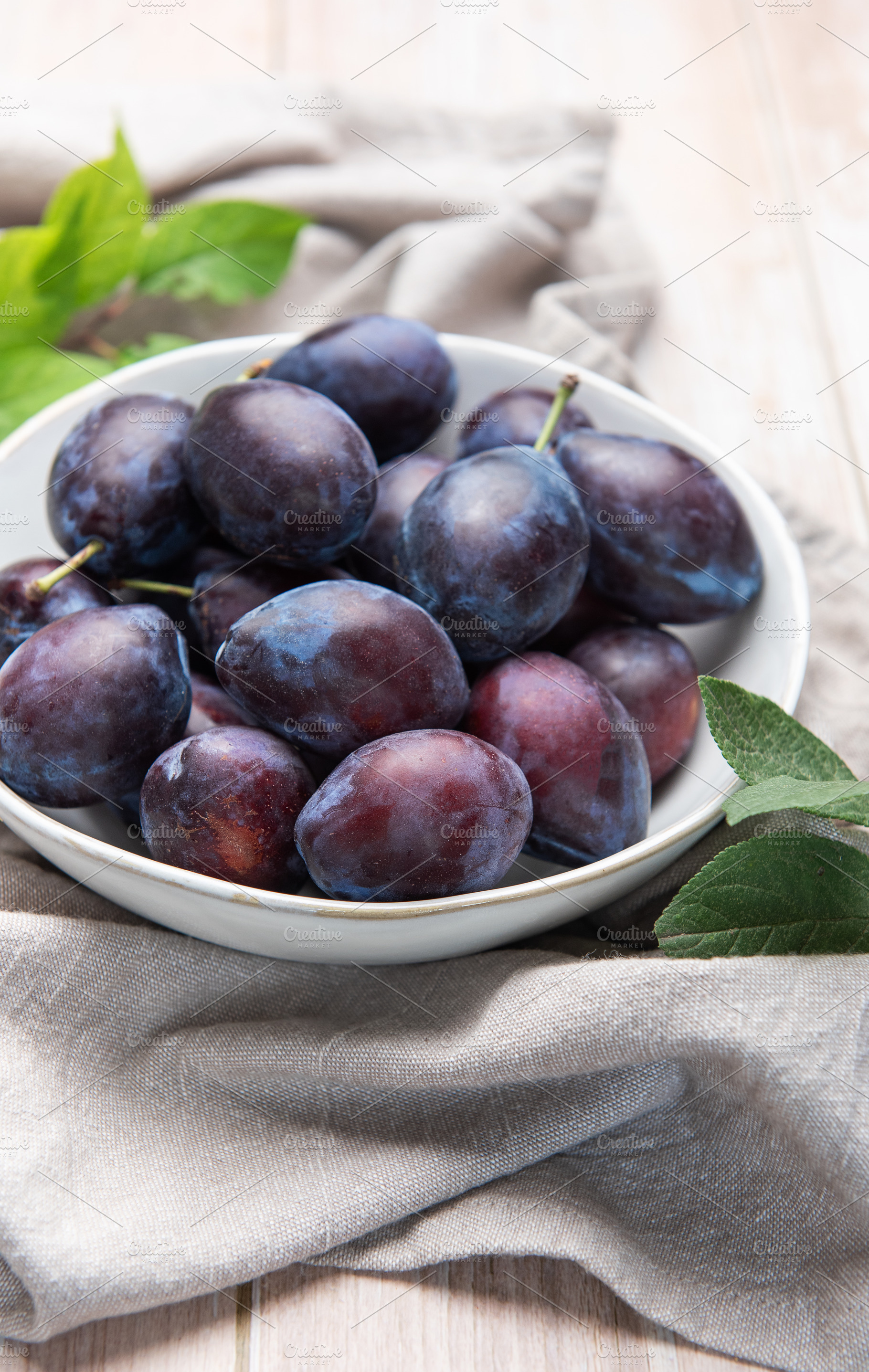 Fresh ripe plums in white bowl on table, a Food & Drink Photo by Olena Rudo