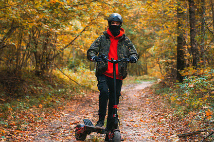 A man rides a powerful electric scooter on forest autumn roads, a Holiday Photo by PavelKant