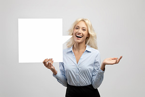 Excited businesswoman holding empty speech bubble, standing over light grey stu, a Photo by Prostock-Studio