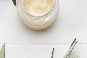Moisturizing cream surrounded by olive branches on white surface, a Health & Medical Photo by Olena Rudo