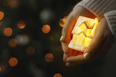 Little glowing house in hands on background of christmas tree li, a Holiday Photo by Sonjachni