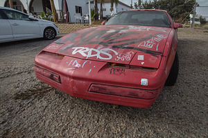 Graffitied red sports car on gravel in urban setting, a Transportation Photo by DanFLCreativo