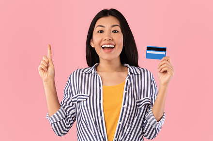 Excited asian woman holding credit card pointing up, a Background Photo by Prostock-Studio