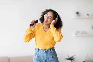 Cool karaoke or music app. Beautiful black woman in wireless headphones using s, a Photo by Prostock-Studio