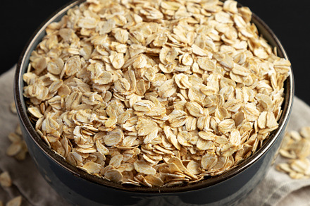 Wholegrain Oat Flakes in a Bowl on a black background, side view, a Food & Drink Photo by LiudmylaChuhunova