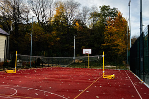 Autumn outdoor volleyball court scene with net, red surface and colorful trees, a Photo by AS photostudio