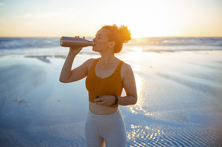 fit sports woman at beach at sundown drinking water, a Person Photo by Alliance Images