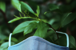 A blue fabric face mask mockup hanging against a backdrop of green leaves, a Mask Mockup by Textures & Backgrounds