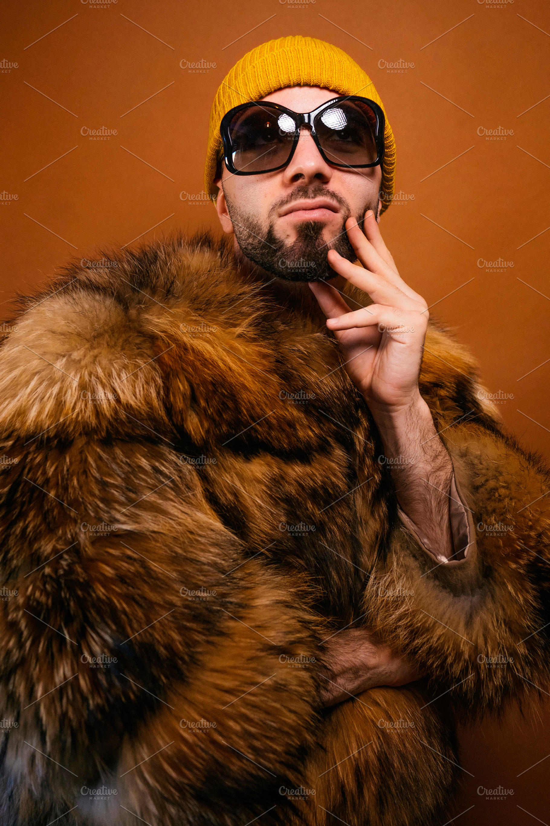 Man wearing fur coat, yellow beanie, and sunglasses, a Photo by karrastock