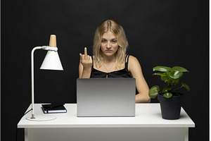 Angry young woman at desk showing, a Business Photo by volodymyrshtun13795