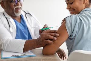Black Woman Receiving Coronavirus Vaccine Injection Sitting With Doctor Indoor, a Photo by Prostock-Studio