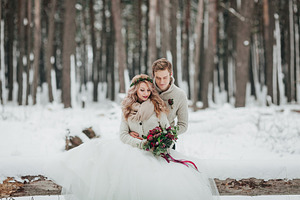 Bride and groom are sitting on the log in the winter forest. Close-up. Winter wedding ceremony.