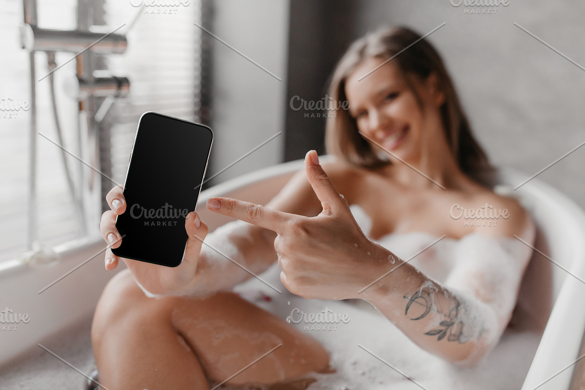 Lady holding smartphone and pointing at blank screen, showing ad, relaxing in f, a Photo by Prostock-Studio (Photo 1 of 2)