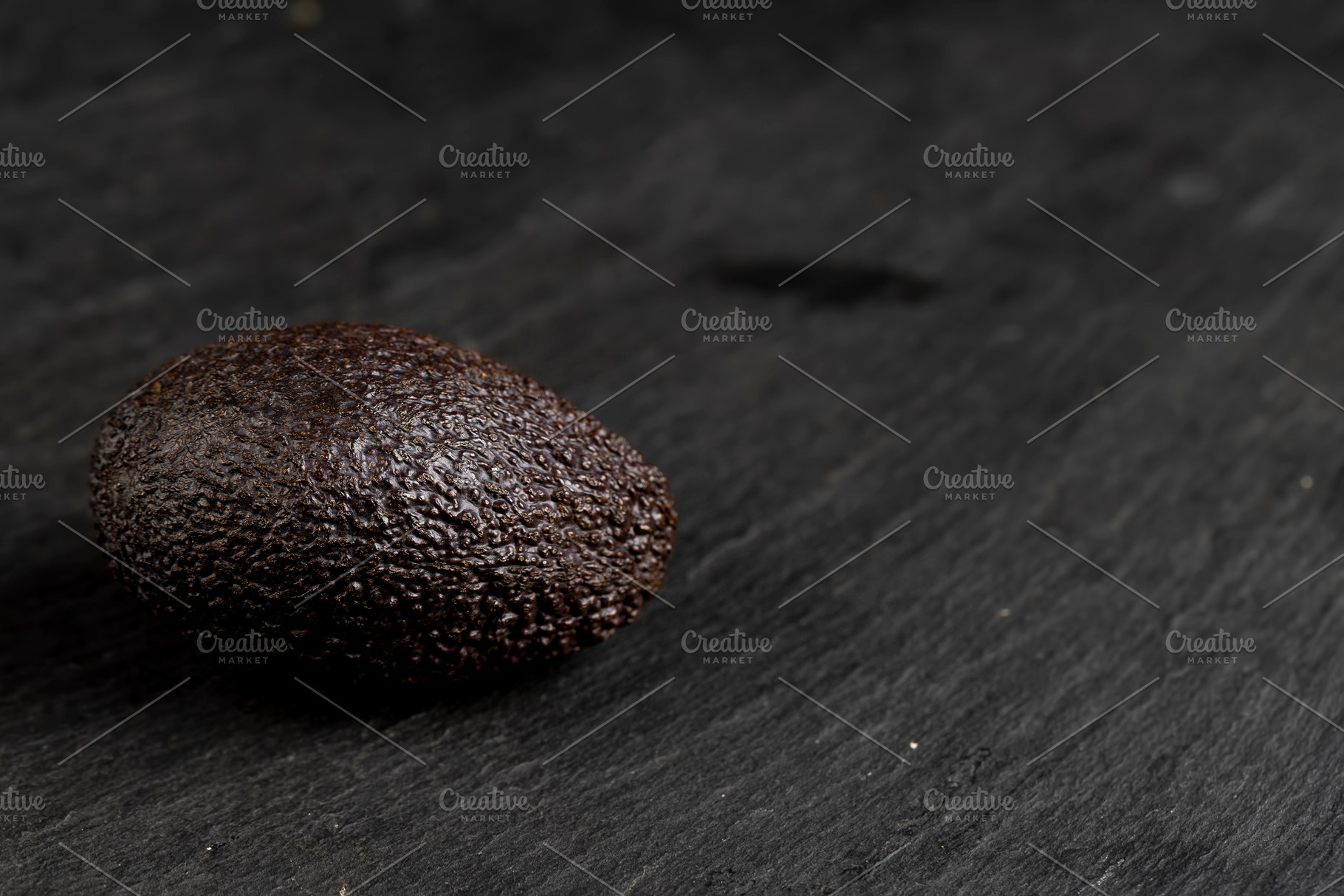 several whole black avocado fruits of small size on a black slate, a Photo by rsoollAI
