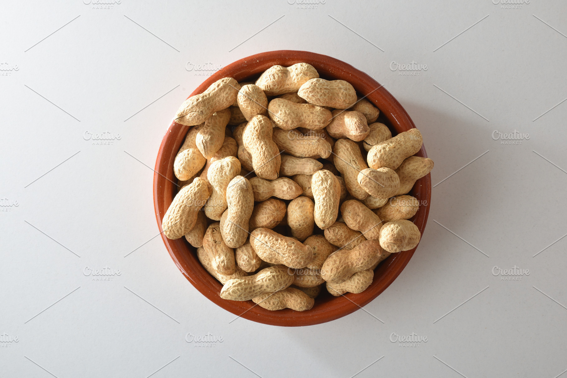 Heap of peanuts with skin in clay bowl on table, a Food & Drink Photo by Davizro's Market