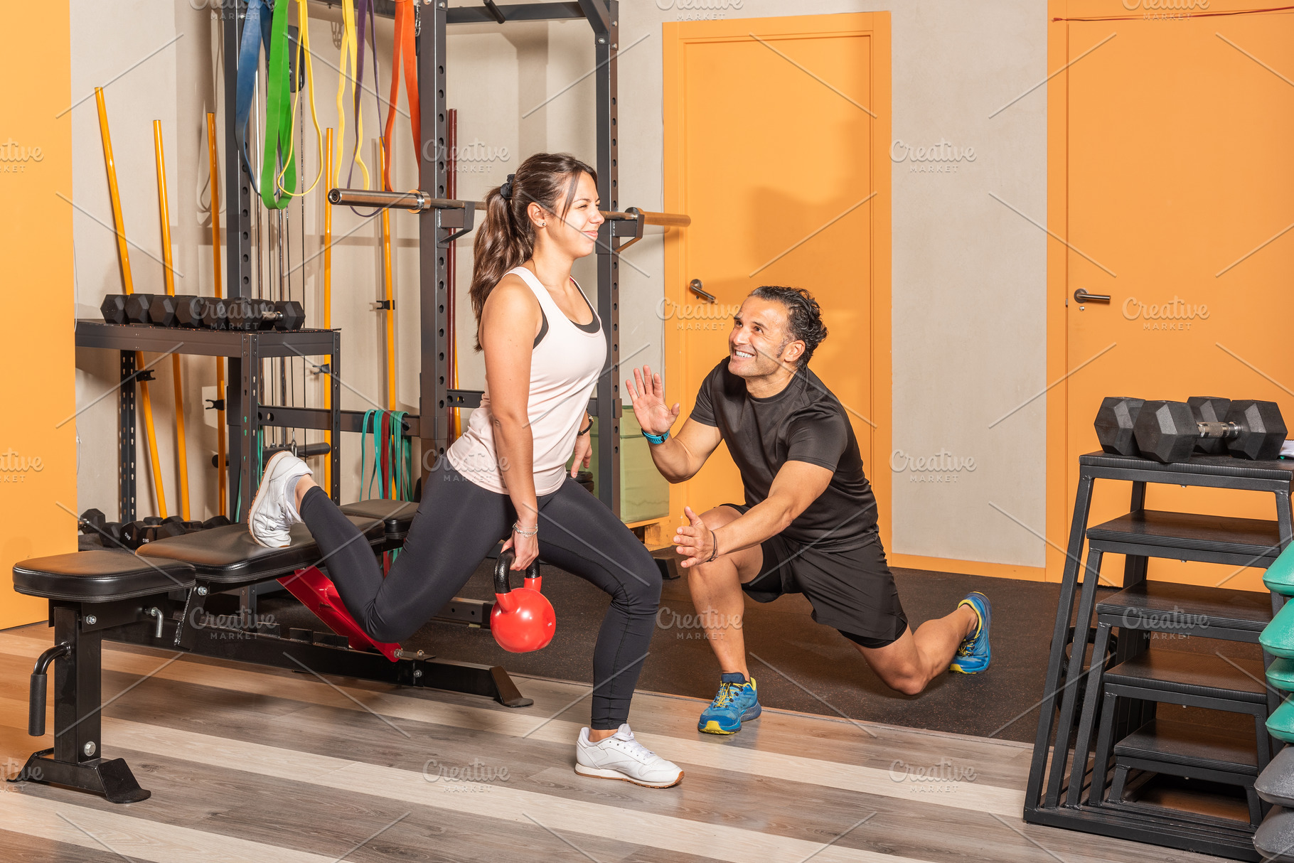 Woman doing lunges with a kettlebell with help of coach with one leg resting on, a Sports & Recreation Photo by Iván Moreno STOCK PHOTO