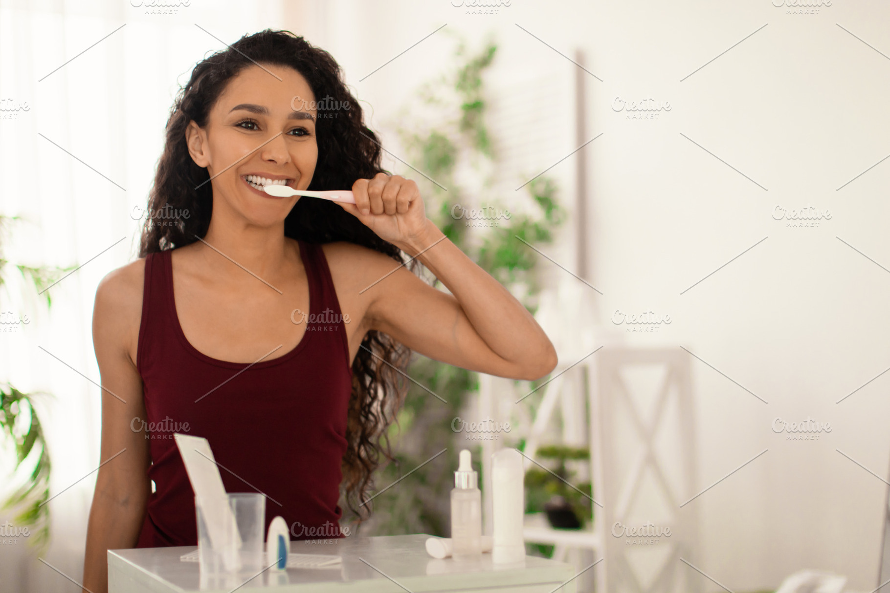 Pretty young woman brushing teeth with toothpaste near mirror at home, copy spa, a Photo by Prostock-Studio