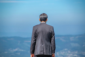 Man in suit facing distant mountains alone, a Person Photo by DanFLCreativo