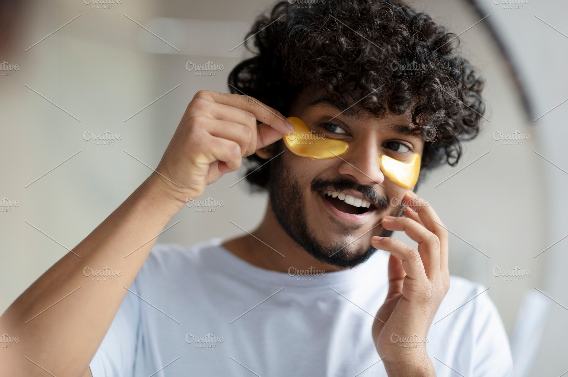 Skin care to reduce eye bags. Cheerful indian man applying gold anti-fatigue pa, a Person Photo by Prostock-Studio