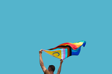 man is waving a progress pride flag outdoors, a Person Photo by Nito